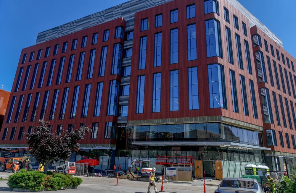 Red-brick office building under construction with tall blue windows and construction equipment in front.